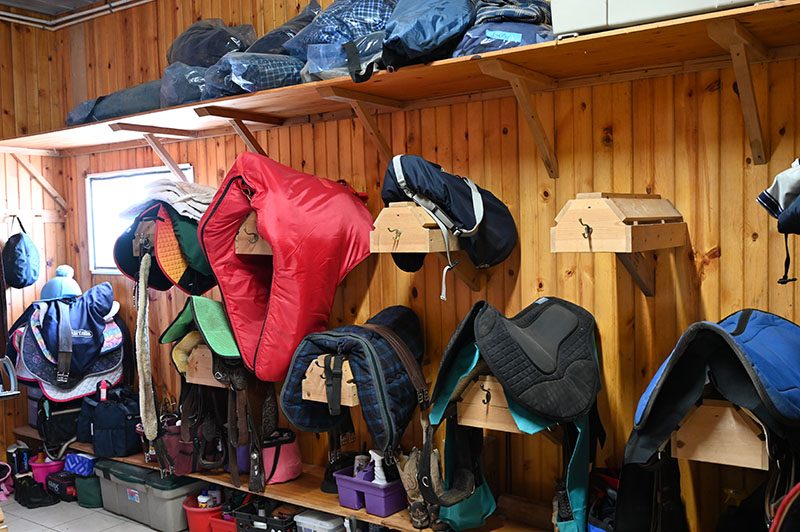 Tack room with saddles on saddle rack and personal storage areas